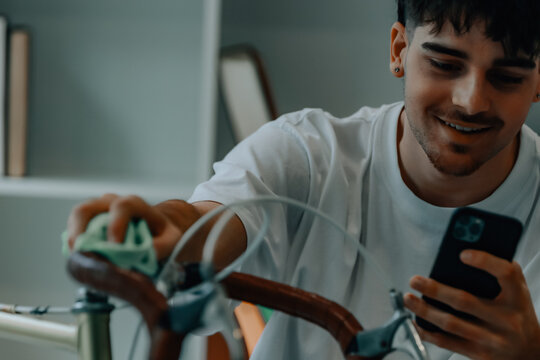 young man cleaning or preparing vintage bicycle looking at mobile phone or app - Powered by Adobe