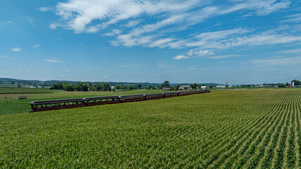 A vintage train rolls along a winding track, surrounded by vibrant green fields under a bright blue sky. The scenic beauty of the countryside enhances the journey, showcasing nature's simplicity.