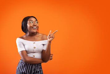 Happy African American Girl Pointing Finger Aside Standing Over Orange Studio Background. Copy Space