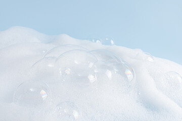 Chic white fluffy foam, soap foam texture with clear bubbles on blue background. A copy space. Layout for advertising detergent, spa cosmetics.