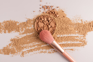 A block of compact powder broken into pieces stands on spilled dry powder with a brush makeup . A sample texture powder in different tones. top view.