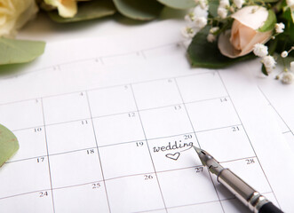 Wedding calendar with pen writing text on planning date on background with roses