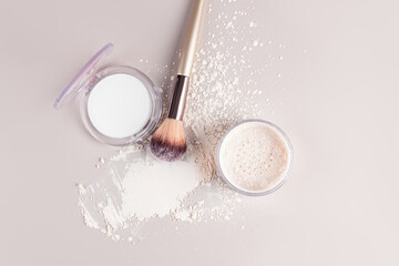 Two open packs of compact and loose powder in a light, white matte tone with a makeup brush and a powder sample on a light background. top view.
