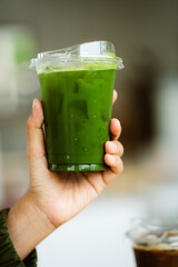 hand of woman holding a take-out iced matcha latte on table at cafe, isolate concept.