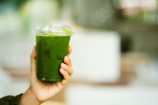 hand of woman holding a take-out iced matcha latte on table at cafe, isolate concept.