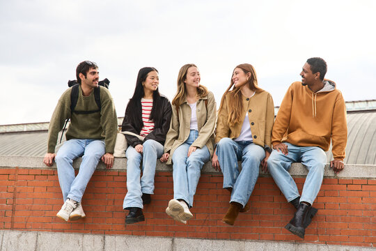 Group of diverse students relaxing and chatting on a brick wall, multiethnic people