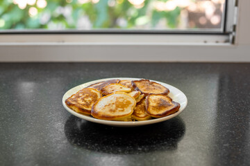 A plate of golden pancakes sits on a countertop by the window, ready to eat
