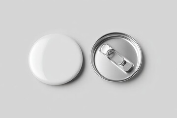 Two overlapping round pin button badges, one showing a blank white front surface, the other showing a metallic back with pin clasp, placed on a smooth light gray background