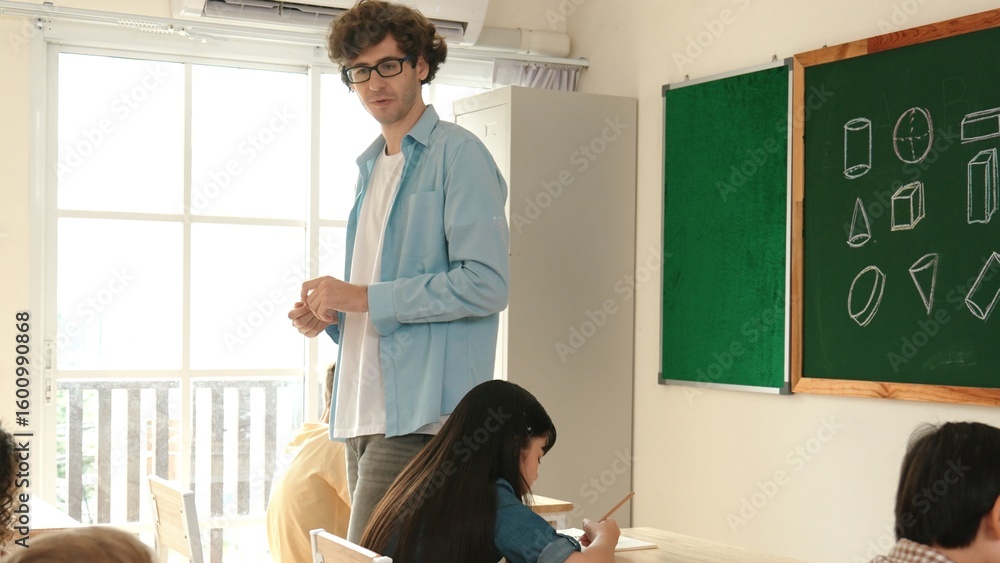 Poster skilled teacher walking at classroom while looking at student homework. professional instructor chec