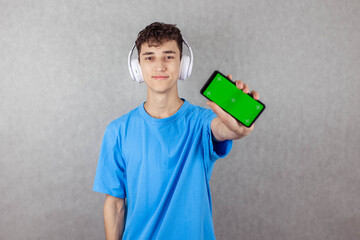 Portrait of Young Guy on Gray Background in Headphones and With Green Screen Phone, Copy Space,...
