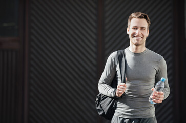 Guy with bottle of water ready for training. Smiling athlete in sportswear with bag goes to gym on...