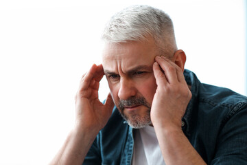 Closeup of mature grey-haired man suffering from migraine at home, touching his temples, panorama...