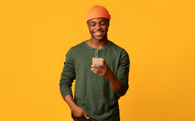 Cool App. Happy young black guy using smartphone, browsing new application or messaging with...