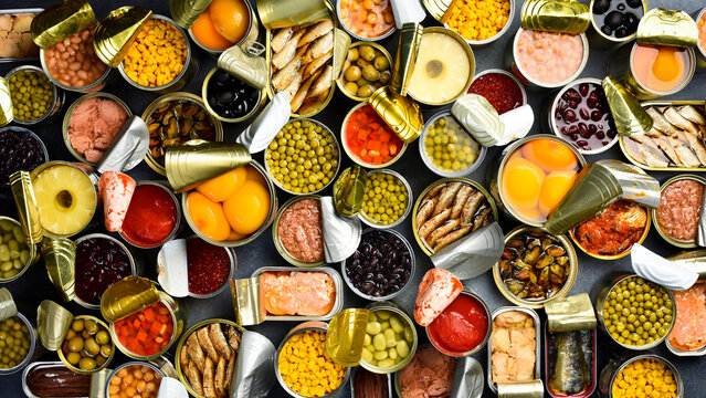 A large set of pickled and canned foods on the background. Metal cans with canned vegetables, beans, fish, seafood and fruit. Top view.