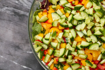 Fresh chopped salad closeup. Colorful mix of cucumber, bell peppers and leafy greens. Healthy raw vegetable bowl on dark marble background. Light vegan lunch idea. No dressing summer food concept 