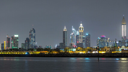Modern Dubai city skyline timelapse at night with illuminated skyscrapers over water surface