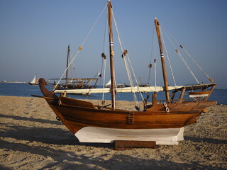 A wooden dhow boat model on a sandy beach.