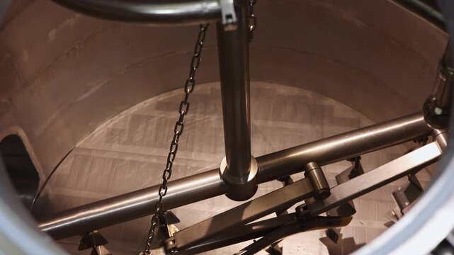 Inside View of Industrial Brewing Mash Tun with Mixer Blades, Close-up footage of an industrial brewing mash tun showing rotating stainless steel mixer blades used in beer production process.
