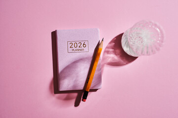 2026 planner, pencil and hourglass against pink background.