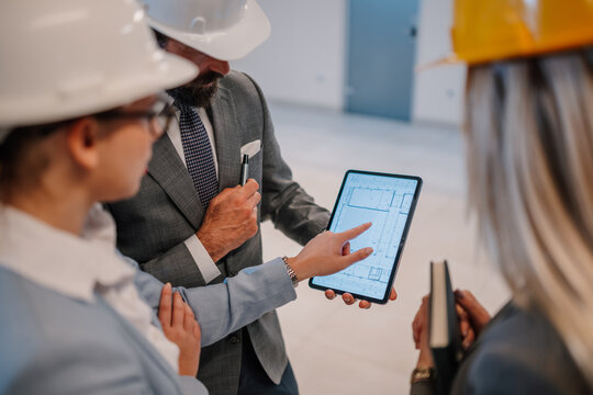 Architects and engineers discussing blueprint on tablet at construction site