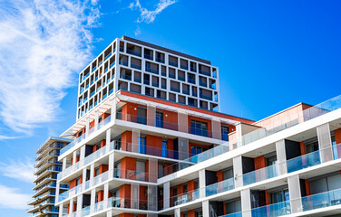 Modern Multi-Story Residential Building with Vibrant Facade, Large Balconies, and Scenic Urban Skyline under Clear Blue Sky