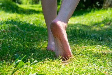 Close-up, beautiful female legs walking barefoot on the green grass summer. Selective focus