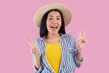 Good Mood. Portrait of joyful young asian woman in summer straw hat showing two victory sign or...