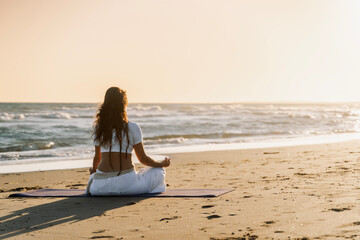 Woman meditating on beach during sunrise