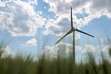 Single wind turbine silhouetted against bright blue sky with scattered fluffy clouds and blurred...