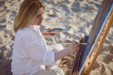 Young woman sits on sandy beach, painting vibrant scene on her canvas. Tranquil setting, with soft...