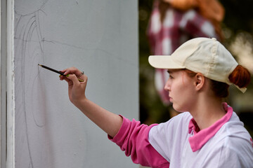 Young caucasian female artist intently sketching on large white canvas outdoors. Soft natural...