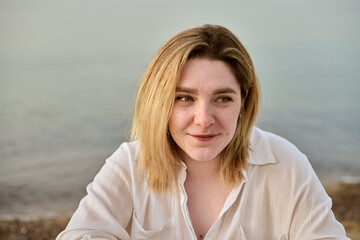 Young woman with blonde hair appears pensive by beach, evoking tranquility and reflection. Soft...