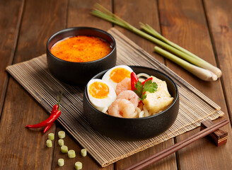 Spicy Shrimp Udon Noodles with Rich Laksa Soup, tofu puffs, fresh chili, and Boiled Eggs in bowl...