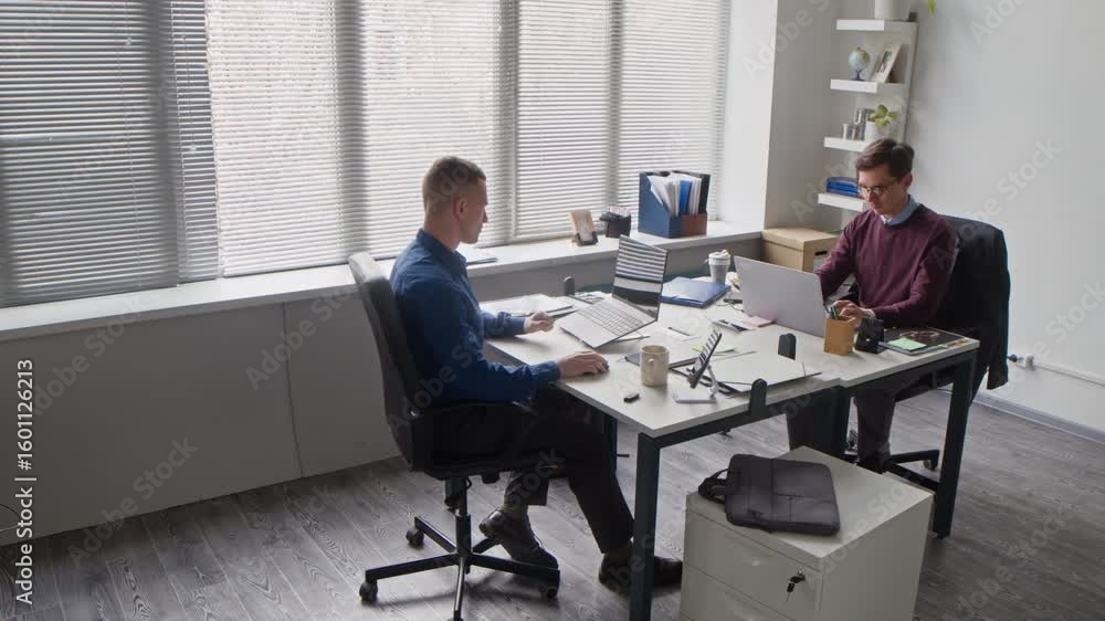 Wall mural pan shot of two focused office employees typing on laptops then passing folder with documents while 