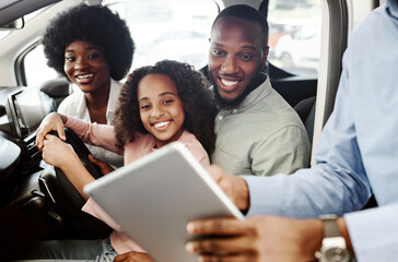 Happy black family testing new car, salesman showing them purchase or lease agreement on digital tablet at auto dealership. Afro clients making deal with manager, buying vehicle at showroom