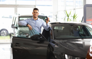 Wealthy middle eastern businessman buying new car in luxury auto showroom, cheerful arab guy...