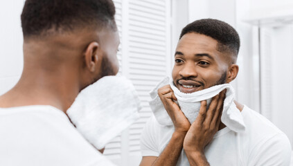 Afro man drying his face after shaving, looking in mirror at bathroom. Metrosexual morning routine...
