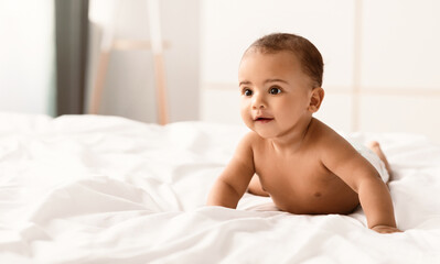 Portrait of a cute little African American baby lying on the white blanket at home. Black naked...