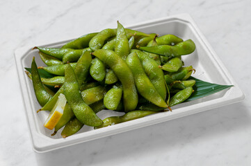 Fresh edamame in a takeout container on a white background. Natural light enhances this healthy Japanese dish, perfect for Asian fusion cuisine lovers