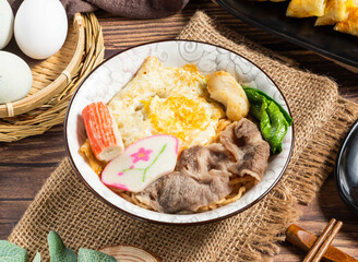 Savory Asian Noodle Bowl with Sliced Beef, Egg, Fish Cake, and Greens in bowl side view of hong...