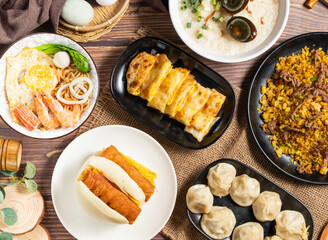 Assortment of Taiwanese Breakfast Dishes with Steamed Buns, Fried Dough Stick, Steamed Xiao Long Bao, Egg Pancake Rolls, Beef Egg Fried Rice, Century Egg, Lean Meat Porridge, Seafood Noodle Bowl