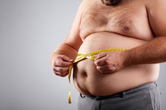 Overweight man measuring belly fat.  Studio shot. Ideal for healthcare, diet, and fitness related marketing.