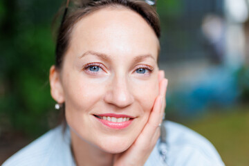 Close-up detail portrait view of young adult beautiful woman holding head chin with hand relaxed smiling sitting outdoors on day light. Female person close natural calm emotions outside