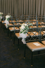 Beautifully decorated chairs with floral arrangements arranged for a wedding ceremony in a spacious indoor venue