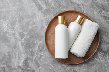 Two white bottles with gold caps and a rolled white towel rest on a circular wooden tray atop a marble surface