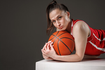 Portrait of confident female basketball player in red uniform with ball in studio, women&rsquo;s sports