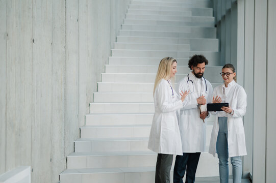 Doctors discussing patient data using tablet in hospital corridor