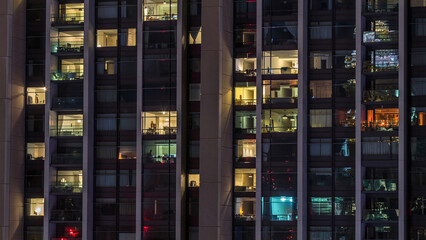 Windows of the multi-storey building of glass and steel lighting inside and moving people within timelapse
