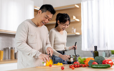 Attractive korean man and woman in casual outfits cooking together at home, making delicious...