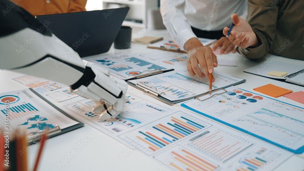 Poster a modern business meeting scene where a robot hand assists human colleagues in analyzing data charts